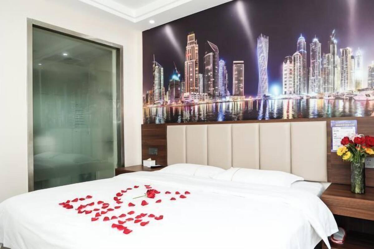 A hotel room with a bed, a cityscape mural, a night sky, and a vase with flowers.