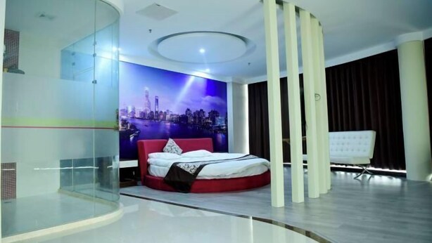 Quarto moderno com parede de vidro curva, mural com vista urbana, luminária de teto circular e cama vermelha.