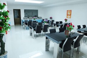 Une salle de conférence avec des tables et des chaises, une plante en pot et une affiche accrochée au mur.