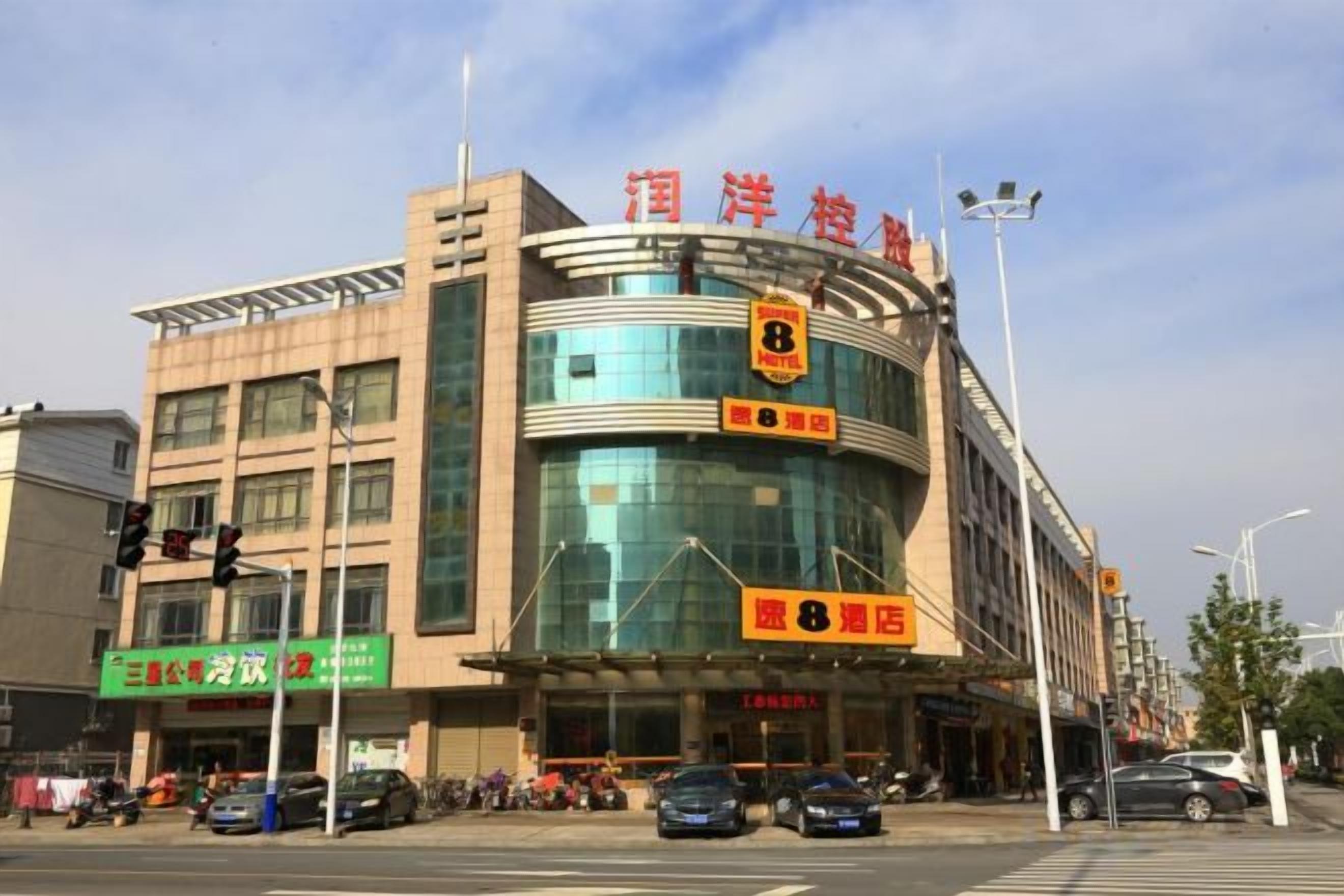 A multi-story building with a curved glass facade, signage indicating a hotel, and a pedestrian crossing in front.