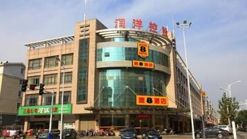 A multi-story building with a curved glass facade, signage indicating a hotel, and a pedestrian crossing in front.