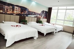 Habitación de hotel con tres camas, un mural de paisaje urbano y un ventanal grande.