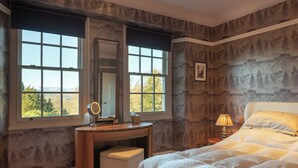 A bedroom with a large bed, a vanity with a mirror, and a window with a view of trees.