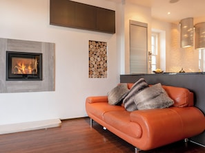 A modern living room with a fireplace, a sofa, and a kitchen area.