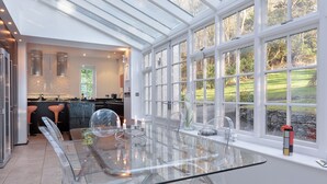 A modern kitchen with a glass dining table, large windows, and a view of the outdoors.
