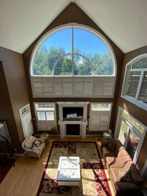 Enjoy the serene view from the high, arched window in this cozy living space, featuring a fireplace, comfortable sofas, and a stylish coffee table.