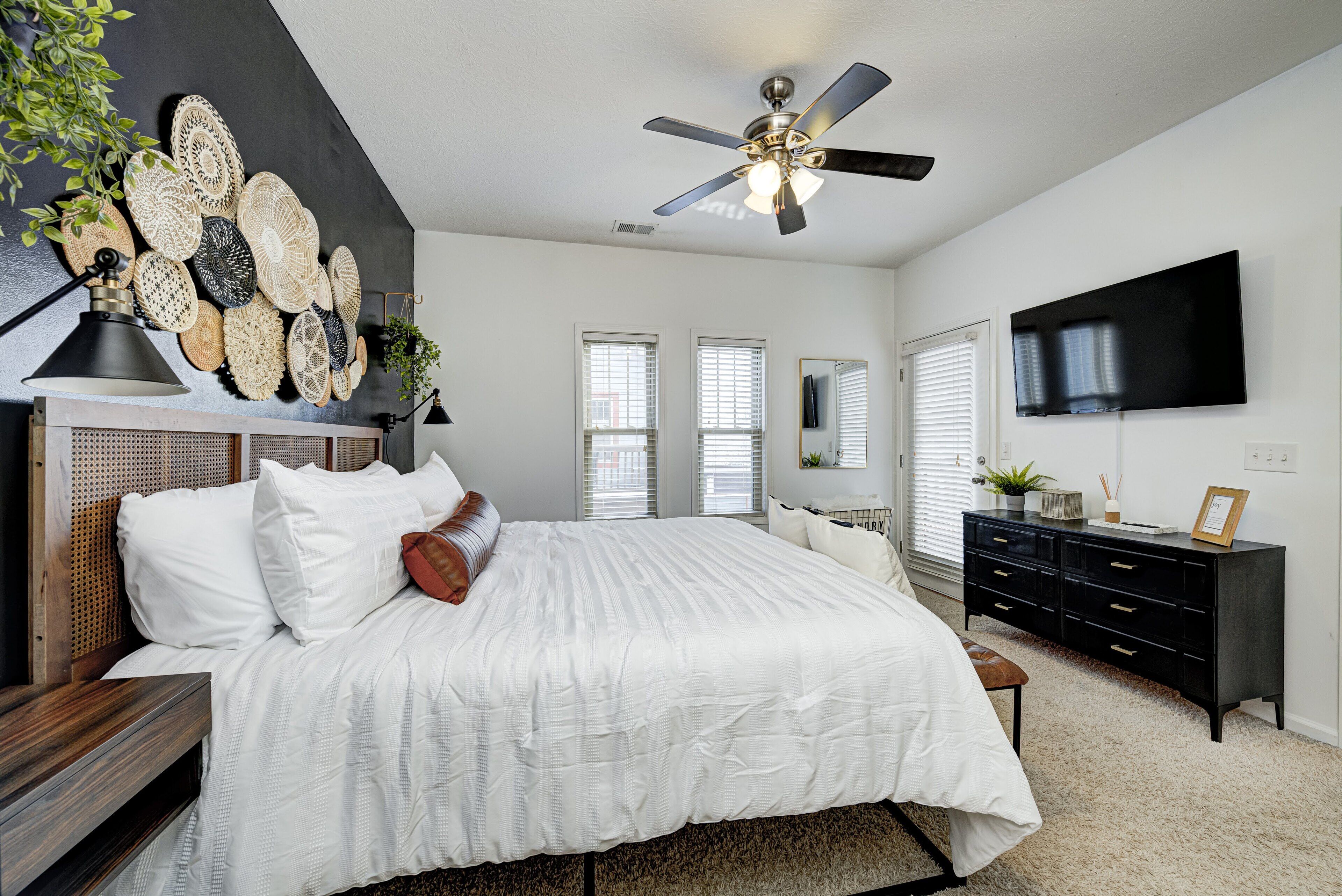 A bedroom with a bed, a ceiling fan, a dresser, and a TV mounted on the wall.