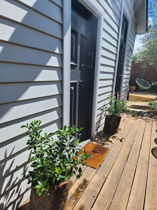 Une terrasse en bois agrémentée de plantes en pot et une porte donnant accès à un bâtiment.