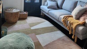 A modern living room with a sofa, a round wooden side table, a green pouf, a patterned rug, and a large abstract painting on the wall. - Jayda- **A split level home with a magical ambience ** (Daylesford)
