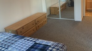 Ein Schlafzimmer mit einem Holzkleiderschrank, einem Bett mit kariertem Überwurf, einem großen Spiegel und einer Schiebetür zu einem anderen Raum.