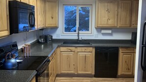 Eine moderne Küche mit Holzschränken, einem schwarzen Kühlschrank, einem Herd und einem Geschirrspüler.