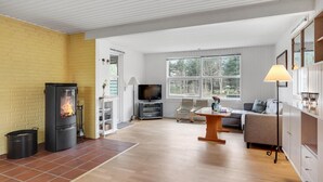 A cozy living room with a fireplace, a television, a sofa, and a dining table. - Beautiful home in Saltum with kitchen (Saltum)