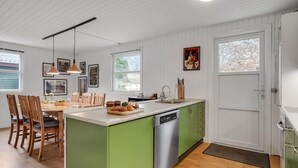 A kitchen with a green island, wooden chairs, a dining table, and a white door. - Beautiful home in Saltum with kitchen (Saltum)