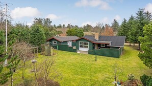 A green house with a red roof, surrounded by a grassy yard and trees. - Beautiful home in Saltum with kitchen (Saltum)