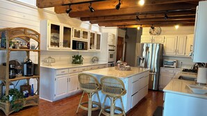 A kitchen with white cabinets, a central island with two wicker chairs, a microwave, a refrigerator, and a stove. - Waterfront retreat with boat dock & private ramp right off the river (Homosassa)