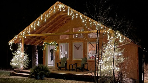 Una cabaña de madera con un porche, luces colgantes y un adorno en la puerta.