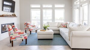 En moderne stue med en hvid sofa, to møblerede lænestole, et sofabord med en plante og store vinduer.