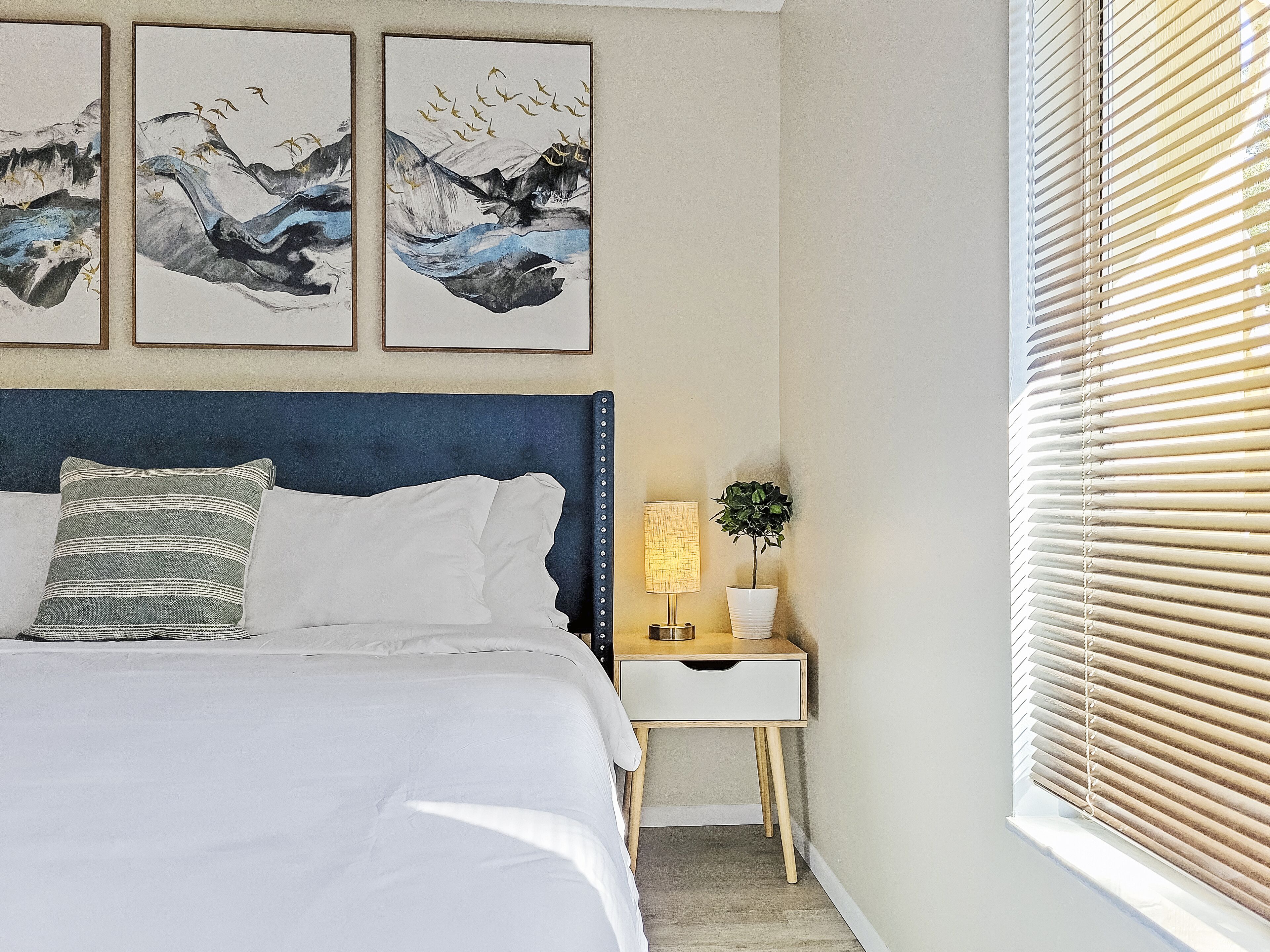 A bedroom with a bed, a nightstand, a lamp, and a window with blinds.