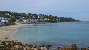 A coastal beach with rocky foreground, clear water, and houses on a hillside in the background. - 3 bedroom awesome home in Plélan-le-Petit (Plélan-le-Petit)