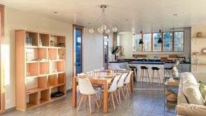 A modern kitchen with a central island, a dining area with a wooden table and white chairs, and a cozy seating area with a sofa and a coffee table. - 3 bedroom awesome home in Plélan-le-Petit (Plélan-le-Petit)