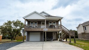 Une maison à deux étages avec un porche à l’avant, un garage et un escalier menant à un balcon situé au deuxième étage.