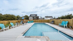 Une piscine rectangulaire dotée d’une terrasse en bois et de chaises longues.