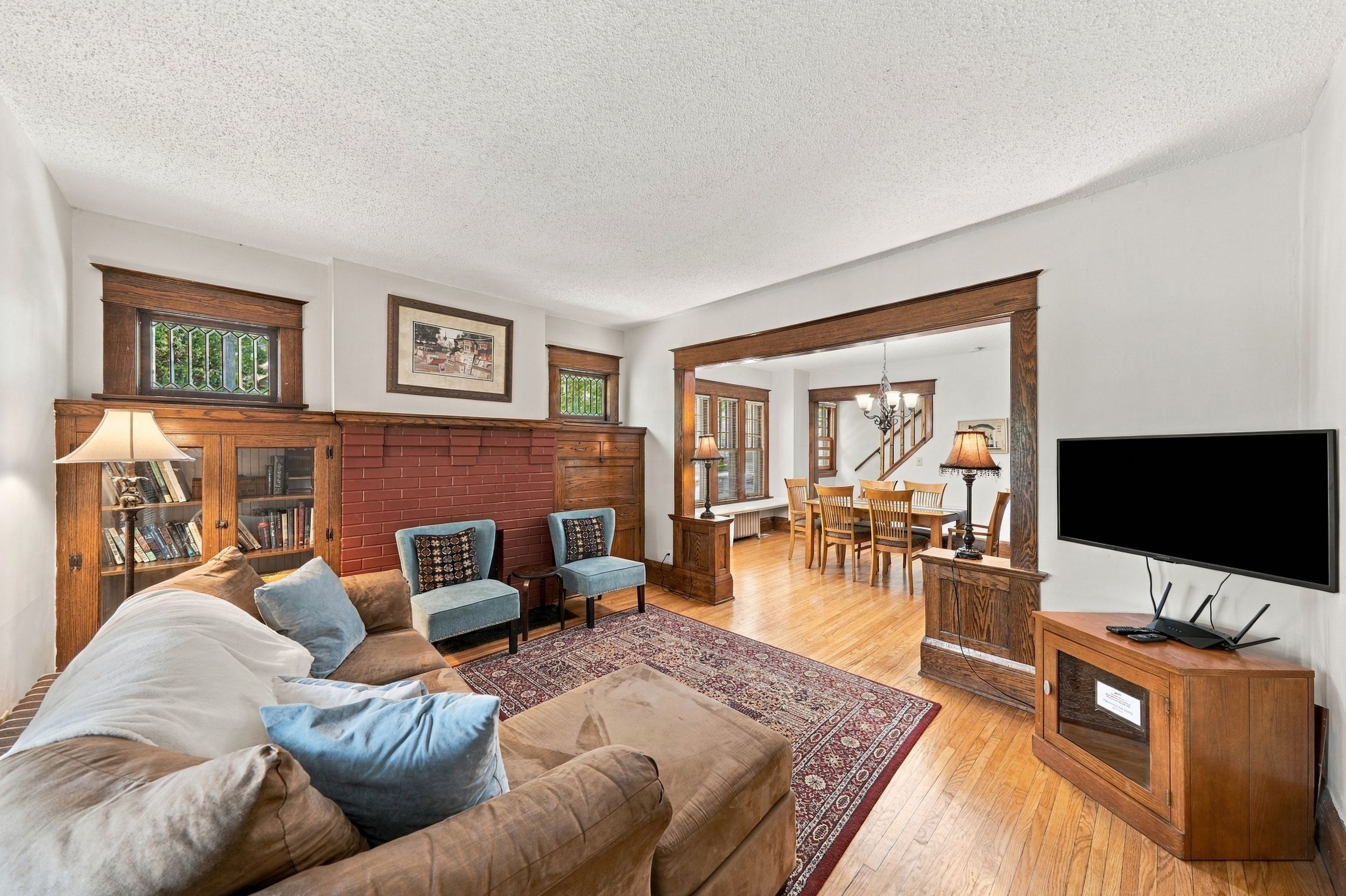 A living room with a fireplace, a sofa, two armchairs, a dining area with a table and chairs, and a TV.