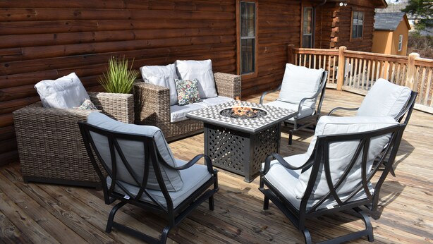 A wooden deck with wicker furniture, a fire pit, and a cabin in the background. - Cozy log cabin, centrally located with covered storage for an RV/Boat (Stanley)