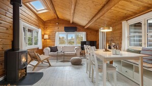 Een knus interieur van een blokhut met een houtkachel, een bank, een eettafel en een televisie.