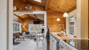 Een gezellig houten interieur met een eethoek, een keuken met fornuis en een raam met uitzicht op groen.