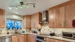 A modern kitchen with wooden cabinets, a stainless steel dishwasher, a built-in oven, a toaster, and a window with a view of trees. - Single-family home steps from Boulder's Greenbelt (Boulder)