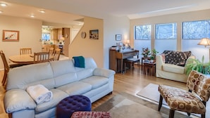 A spacious living room with a sofa, ottoman, and armchairs, a dining area with a table and chairs, a piano, and a kitchen in the background. - Single-family home steps from Boulder's Greenbelt (Boulder)
