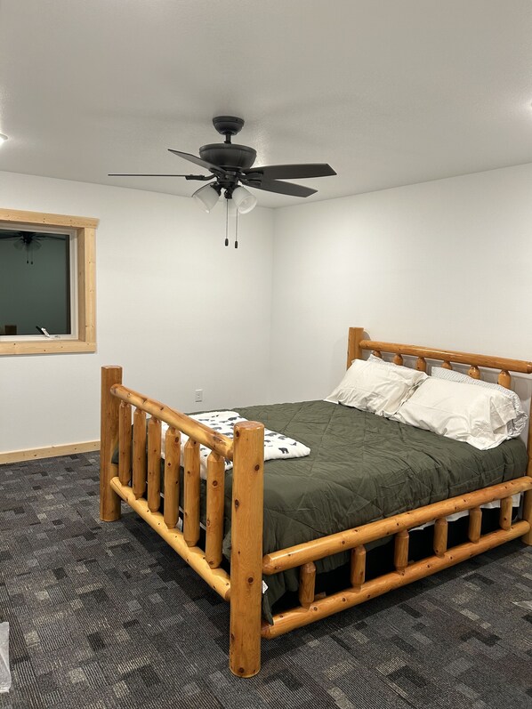 Una cama individual con estructura de madera, un ventilador de techo y una ventana con persianas.