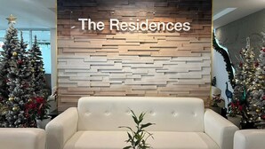 Un interior moderno con un letrero en la pared que dice "The Residences", dos árboles de Navidad y un sofá de cuero blanco.