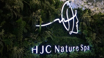Un letrero de neón con el texto 'HJC Nature Spa' en medio de abundante follaje.