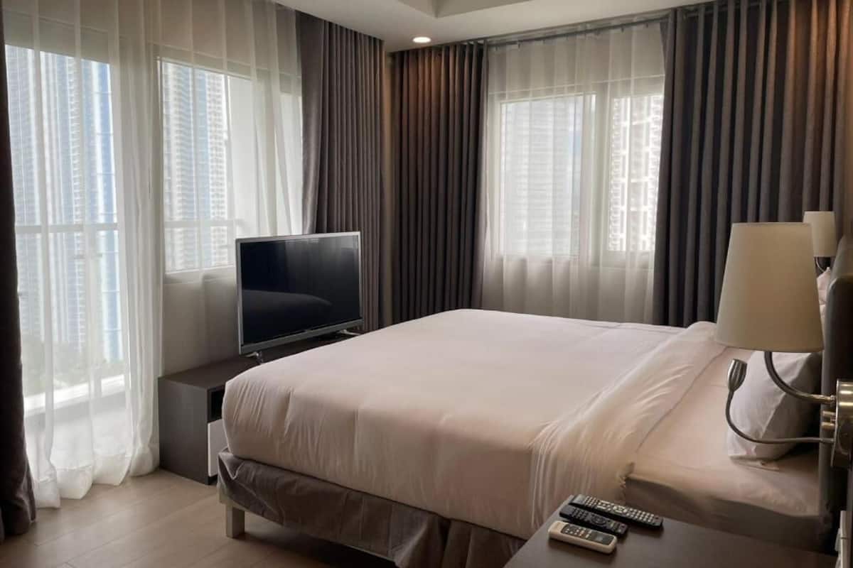 A hotel room with a bed, a TV, a lamp, and curtains.