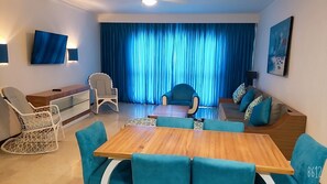A modern living room with a wooden coffee table, teal sofas, and a dining area with chairs.
