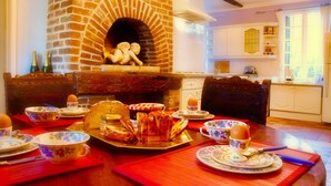 Un coin repas agrémenté d’une cheminée en briques, d’une table en bois et de vaisselle à motifs floraux.