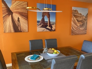 Uma área de refeições com mesa, cadeiras e obras de arte retratando paisagens desérticas.