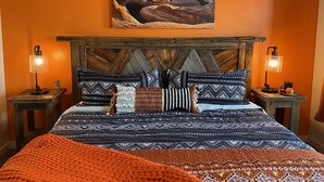 Un dormitorio con una cama grande, almohadones estampados, dos lámparas de noche y un cuadro de un cañón en la pared.