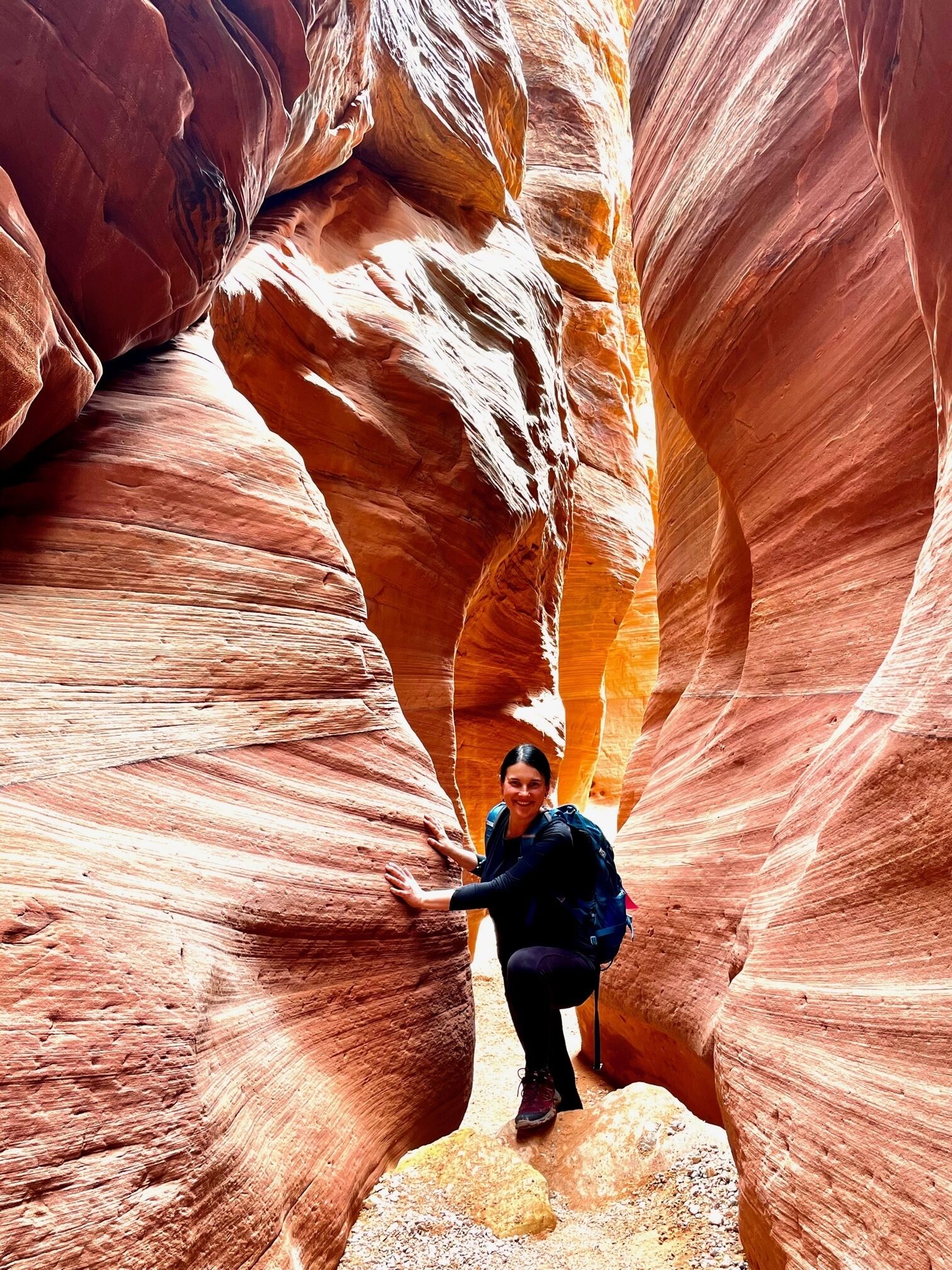 A person crouching in a narrow canyon with red rock walls.