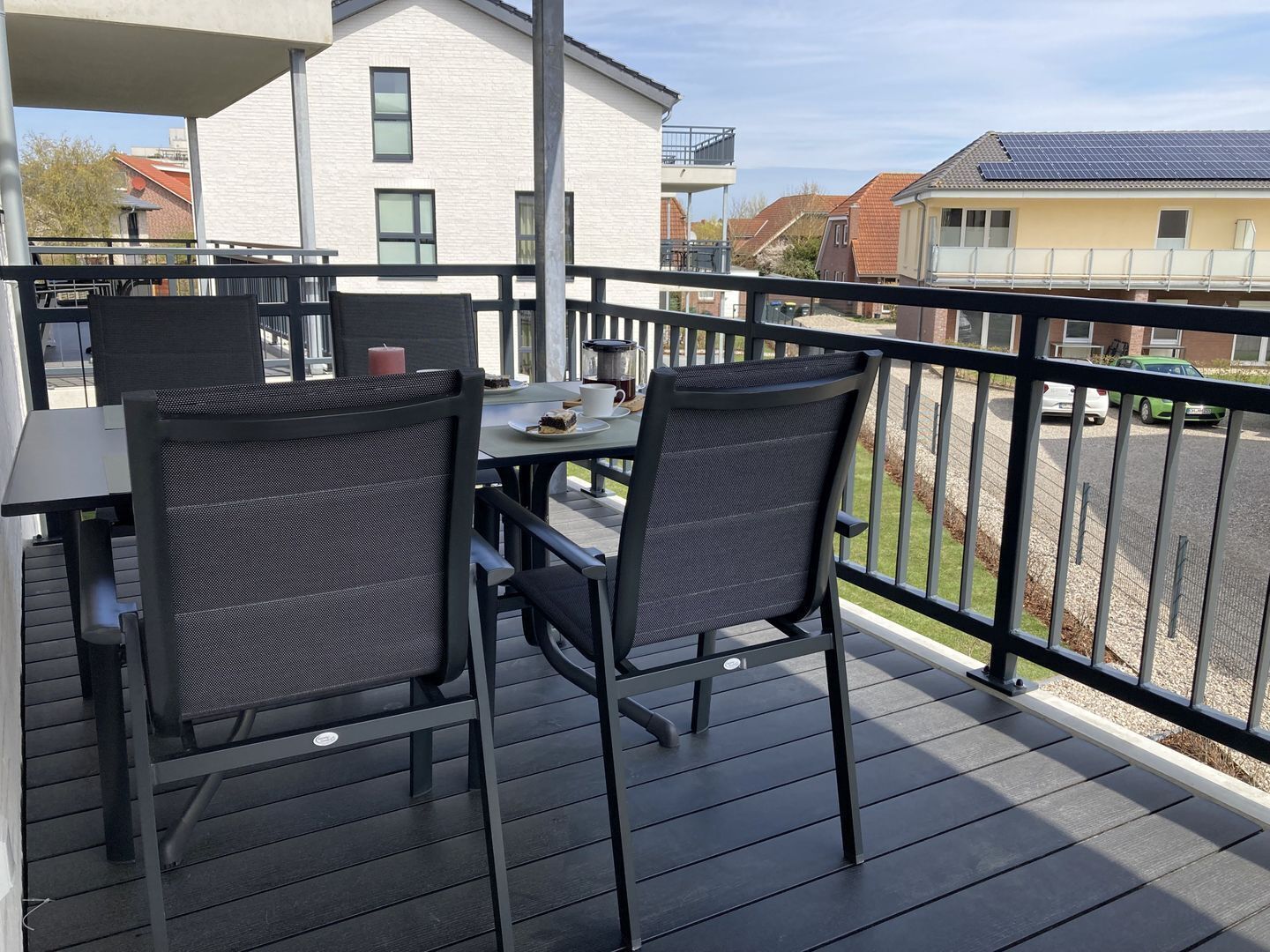 Ein Balkon mit zwei Stühlen und einem Tisch, mit Blick auf eine Wohngegend mit Häusern und einem Auto.