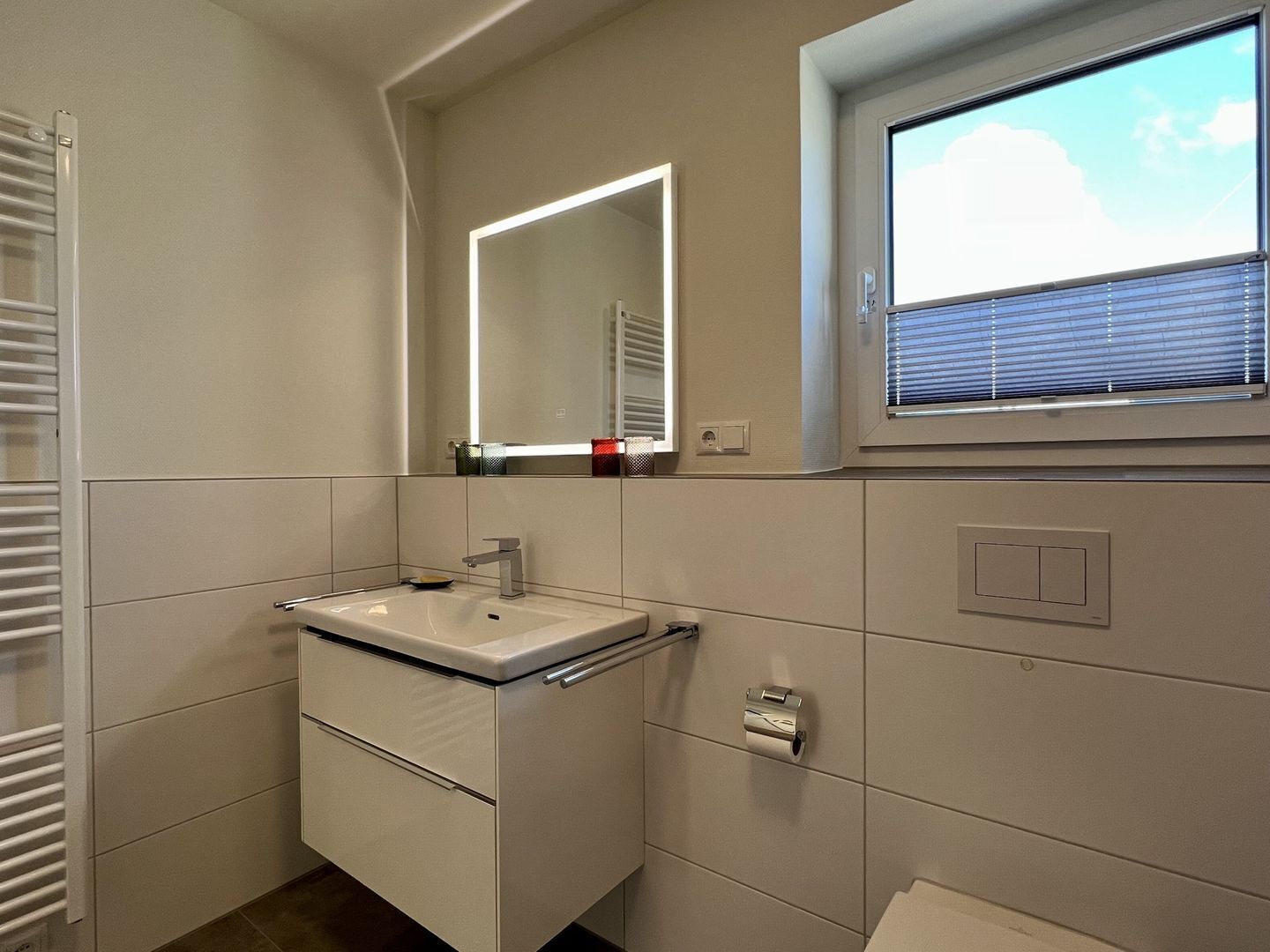 A modern bathroom with a white sink, a mirror, and a window with blinds.