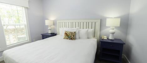 A neatly made bed with white linens, two bedside tables with lamps, and a window with blinds.