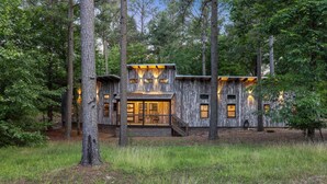 A rustic cabin with a wooden exterior, large windows, and a staircase leading to the entrance. - EV Charger, Peloton Bike, Swing Set, Games, Pets (Broken Bow)