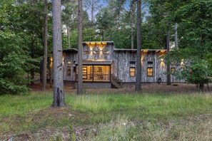 Un chalet rustique avec une façade en bois, de grandes fenêtres et un escalier menant à l’entrée.
