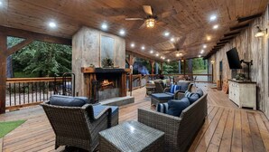 A covered outdoor deck with a fireplace, wicker furniture, and a TV.