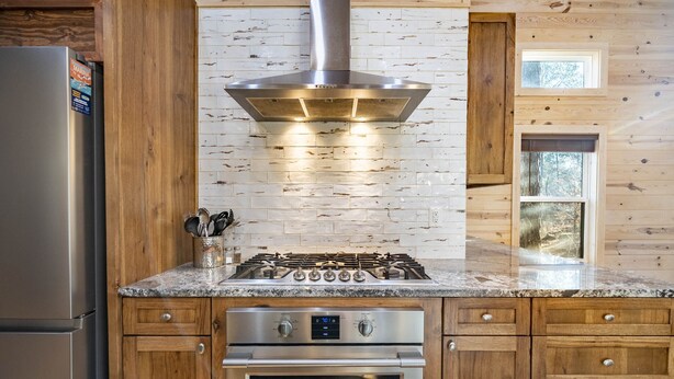 A kitchen with a stainless steel range, wooden cabinets, and a brick backsplash.