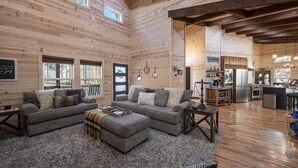 A spacious living room with a large sectional sofa, a fireplace, and a kitchen area visible through an open doorway. - EV Charger, Peloton Bike, Swing Set, Games, Pets (Broken Bow)