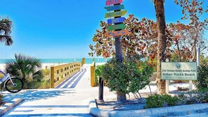 Señal de acceso a la playa con flechas direccionales y una vista despejada de la playa y el océano.